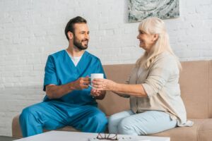 A male nurse holding a cup for an elderly woman in a home setting