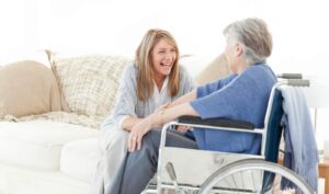 A healthcare provider clasping hands with an elderly person in a wheelchair.
