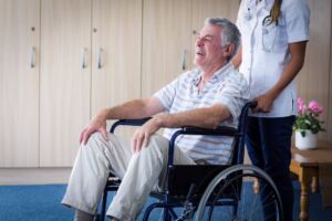 A happy man in a wheelchair supported by a home health care nurse