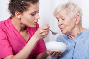 A home health aide blowing at a bowl of soup of an elderly woman